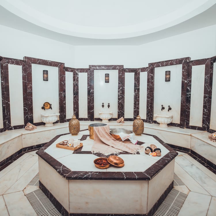Traditional Turkish hammam interior with white marble walls, basins and arched ceiling lit by soft daylight