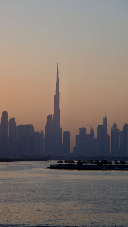 Dubai skyline at sunset with the Burj Khalifa silhouetted against a warm gold and pink sky over calm water