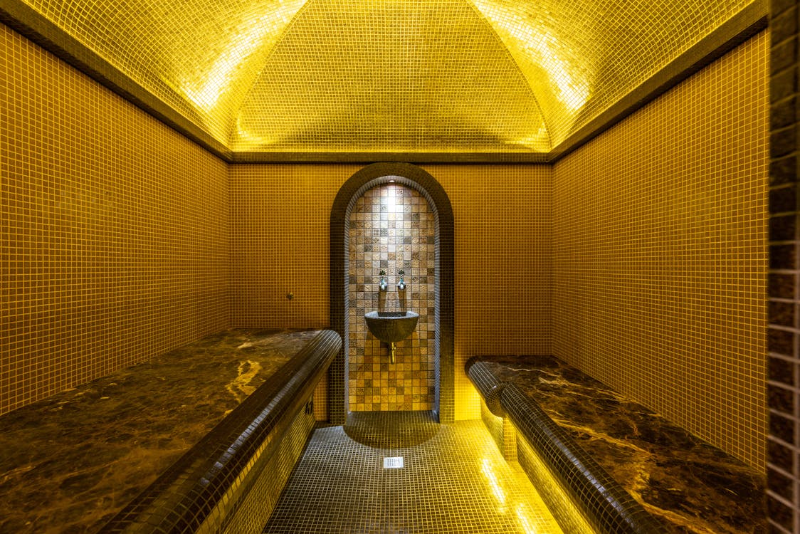 Mosaic-tiled spa wet-zone interior with marble benches and warm golden lighting evoking a Dubai bathhouse